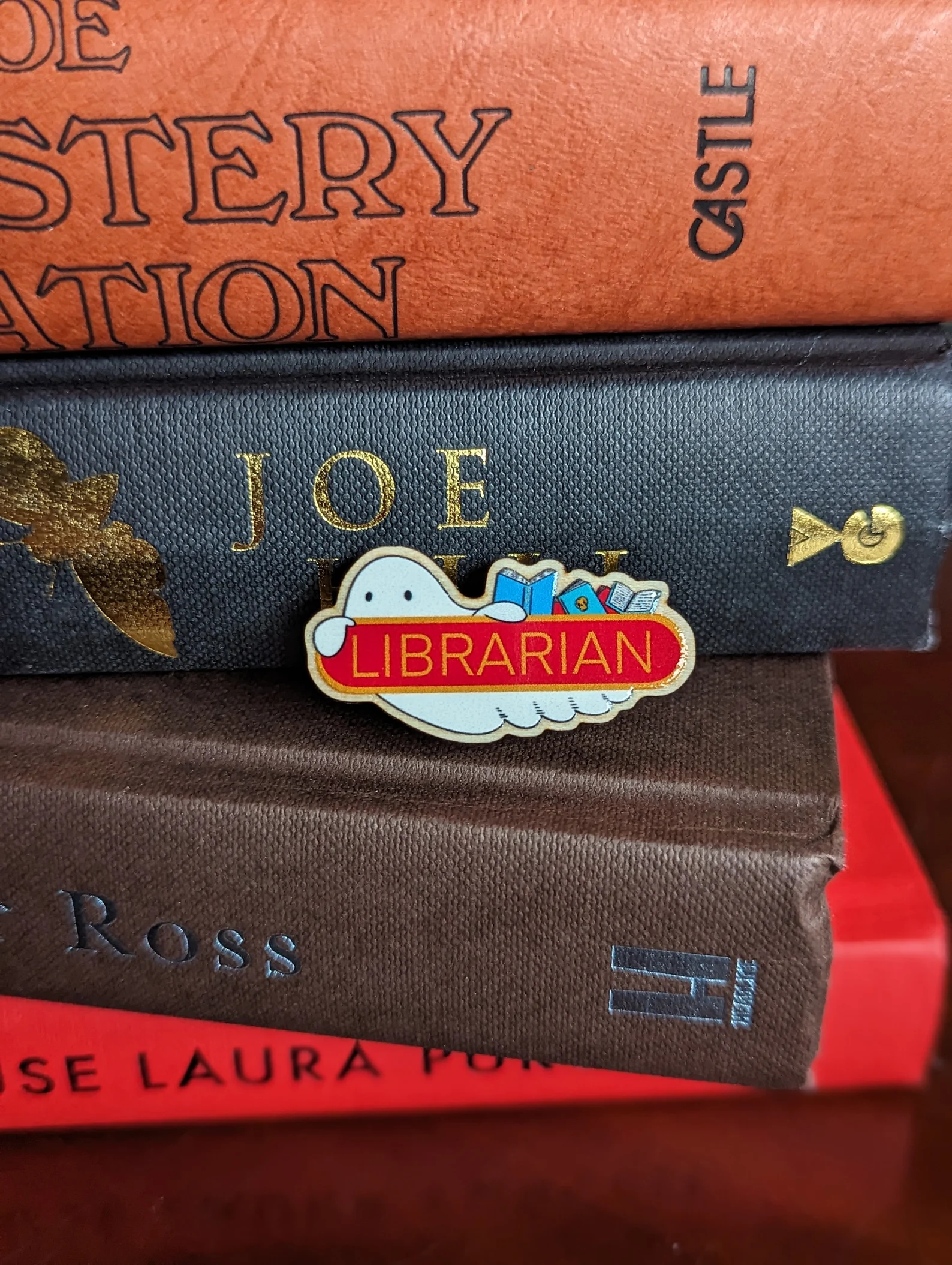 image of a pin that says "librarian," with a ghost and books behind the word. 