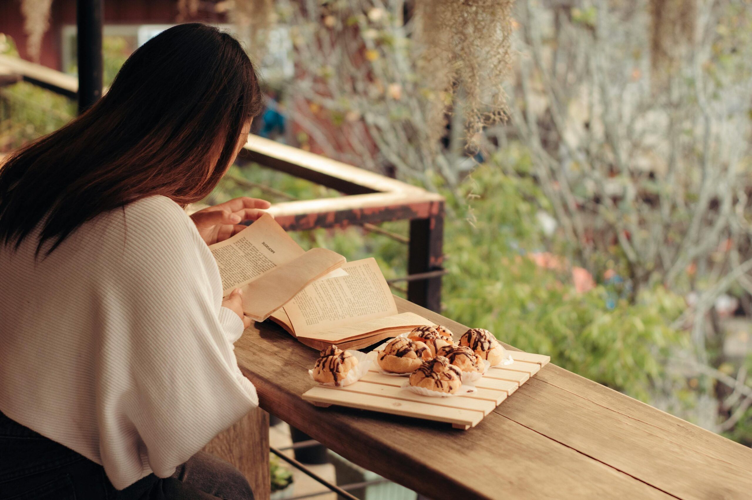 a lightly tanned-skin woman reading with a plate of pastries nearby