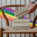 a stack of books with a rainbow watercolor ribbon in the background