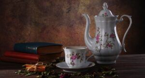 a floral tea pot, cup, and saucer next to a small stack of books
