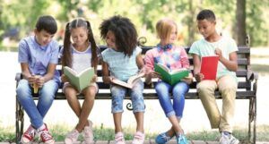 image of several kids of all races reading books on a park bench