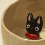 cream-colored ceramic mug with a small black ceramic cat inside it