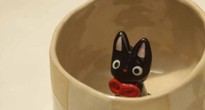 cream-colored ceramic mug with a small black ceramic cat inside it