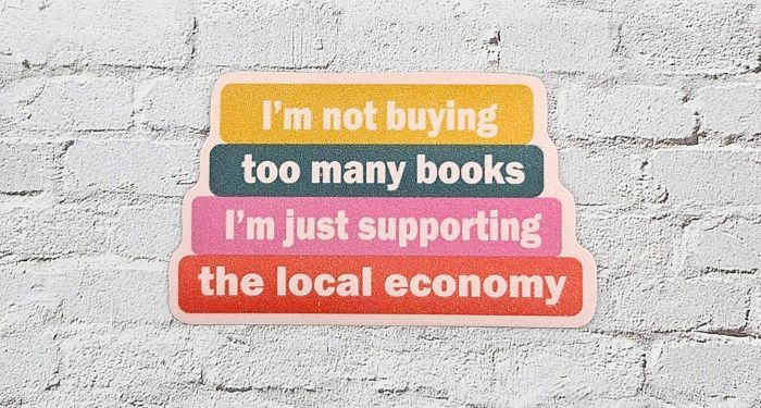 Image of a vinyl sticker designed to look like a stack of books that says "I'm not buying too many books, I'm just supporting the local economy"