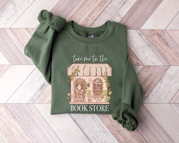 military green crewneck sweater with text that reads "take me to the bookstore" arranged around a graphic of a bookstore front 