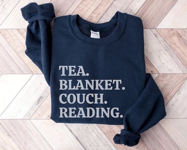 dark blue crewneck sweater with large grey text that reads "tea. blankets. couch. reading."