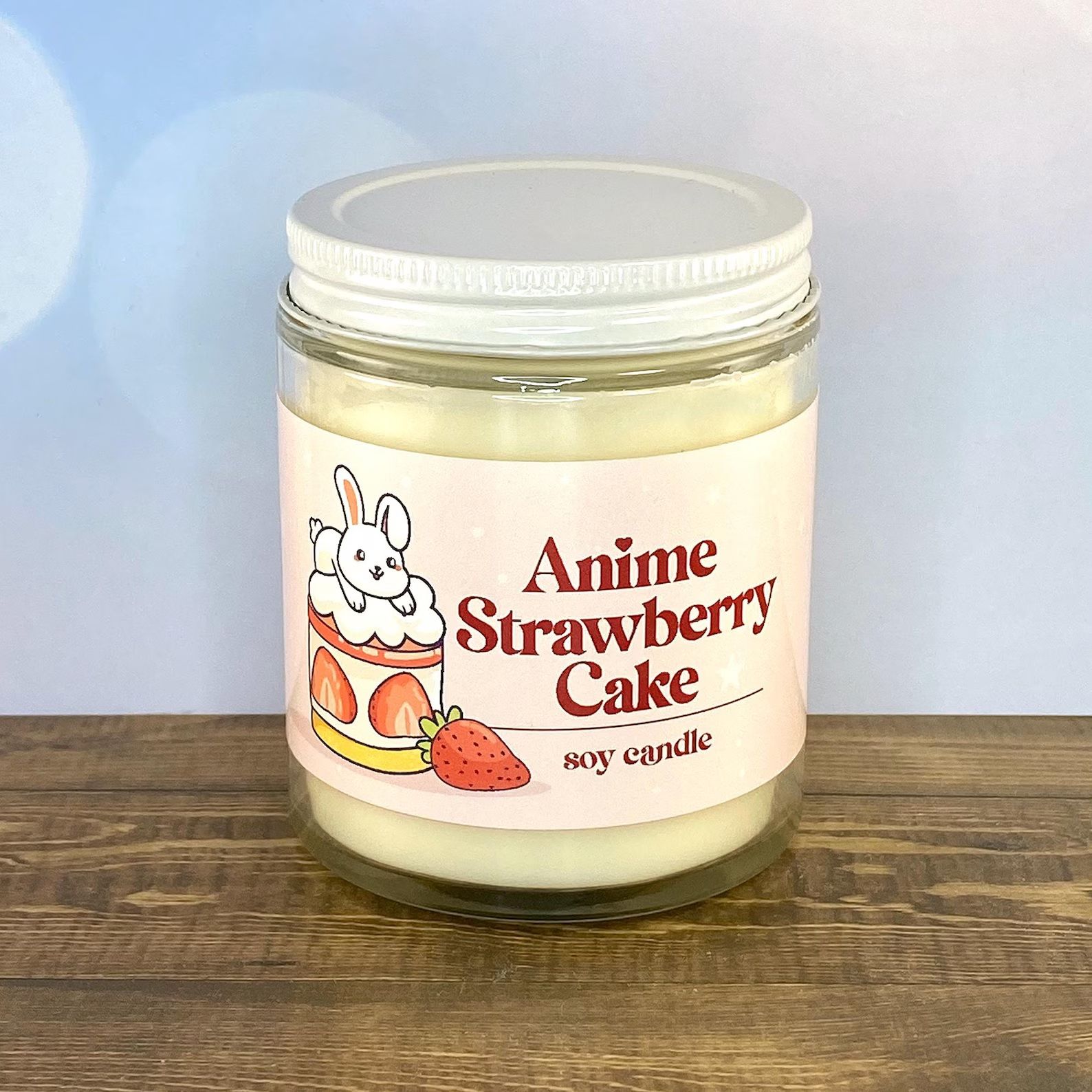 A yellow candle in a glass jar labeled "Anime Strawberry Cake"