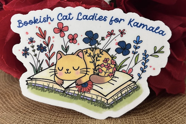 a vinly sticker with an illustration of a cat sleeping on an opened book that says "bookish cat ladies for Kamala"