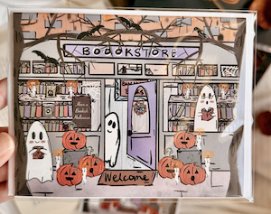 a greeting card with an illustration of a bookstore front window with pumpkins, books, and ghosts shopping