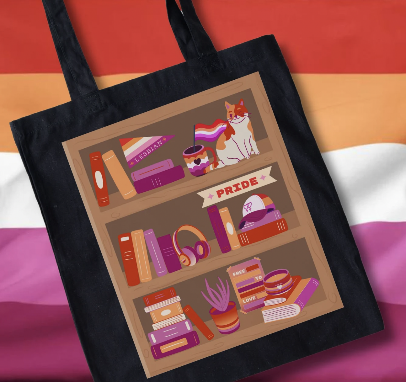 Image of a black tote bag with a graphic print of a bookshelf with books in lesbian pride flag colors