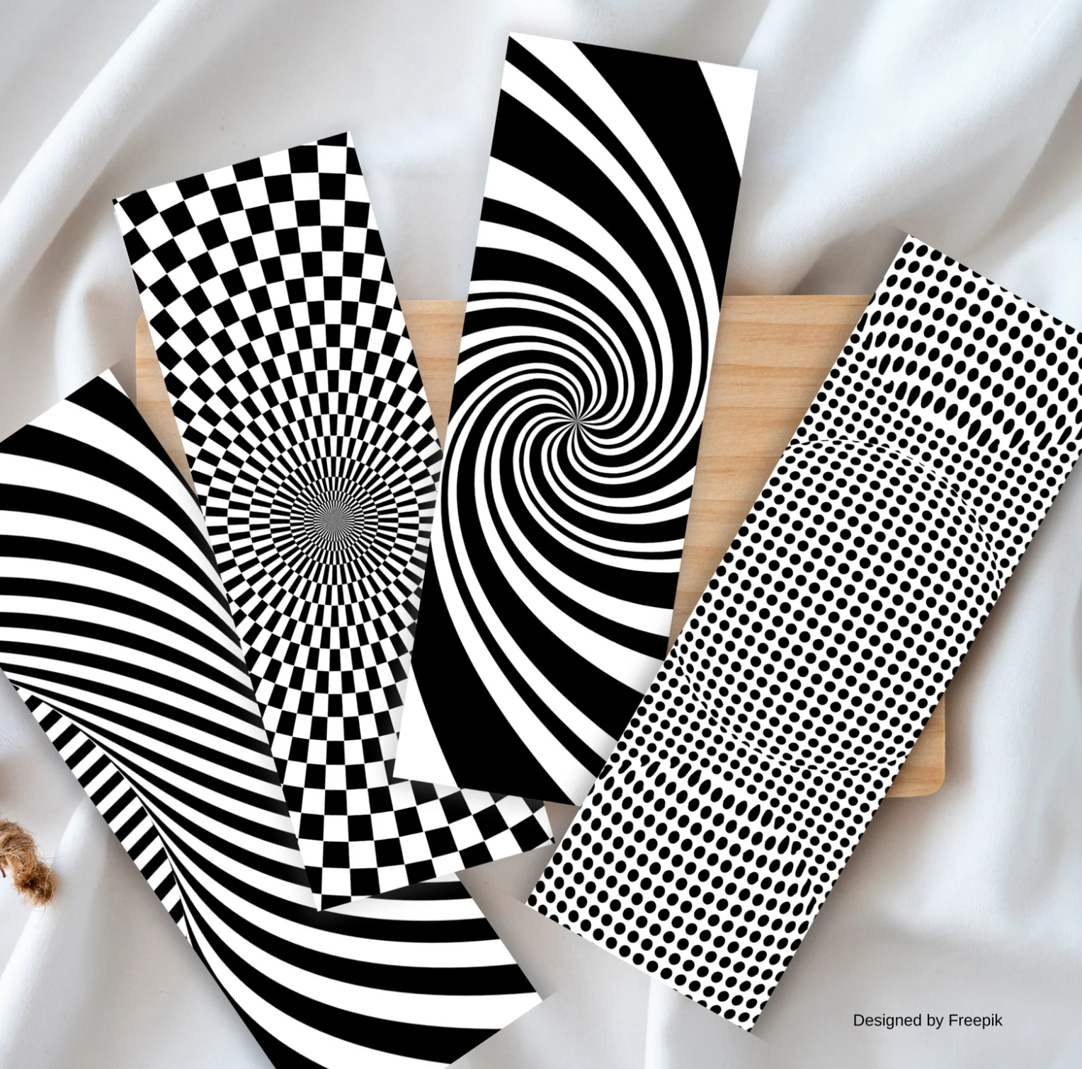 Picture of four bookmarks splayed out against a wooden board and a white sheet. The bookmarks depict various optical illusions in black and white through swirls and dots.