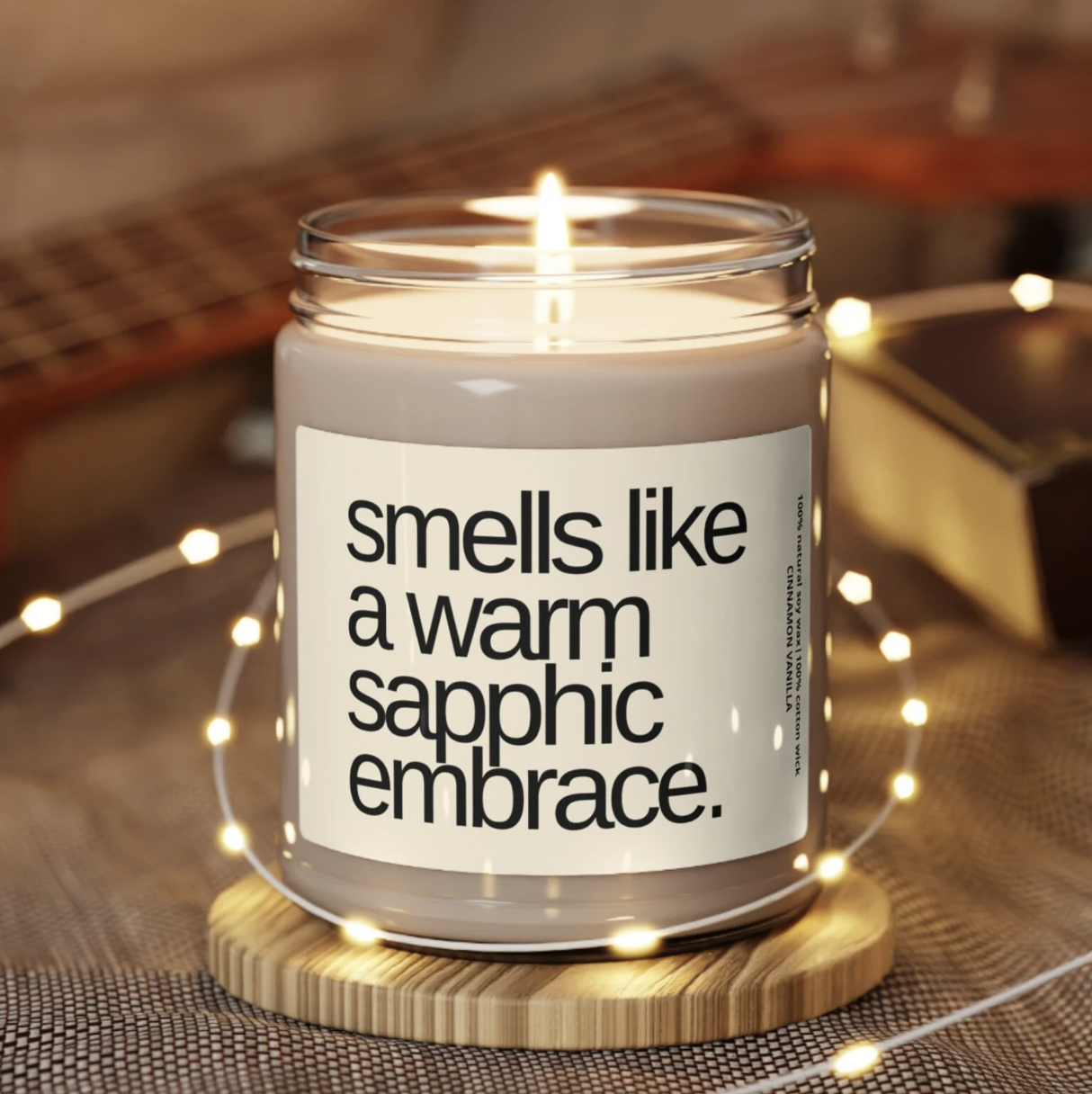 Image of a candle in a glass jar with a label that says "smells like a warm sapphic embrace"