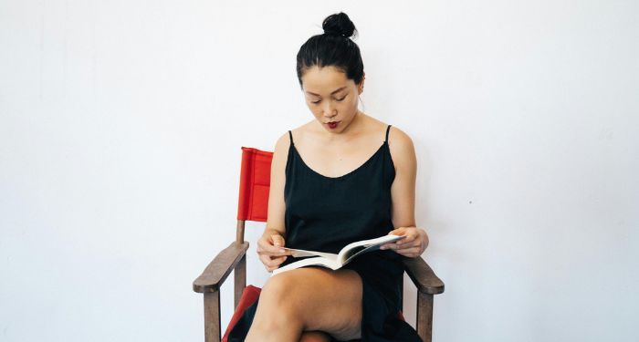 a light tan-skinned Asian woman reading a book in a chair