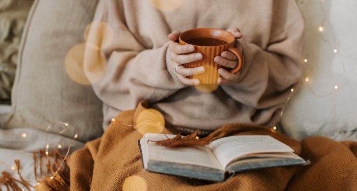 a person wearing a sweater and holding a mug with an open book in their lap