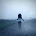 a dark-haired woman levitating on a foggy road
