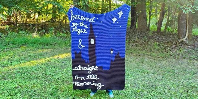 Person holding a peter pan crochet throw up outside in a green yard.