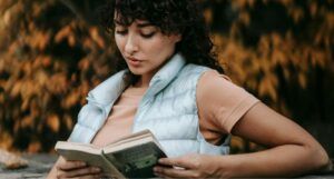 a lightly tanned skin woman reading outside with fall foliage in the background