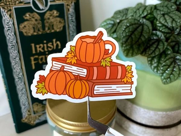 sticker of a small stack of books arranged between leaves and some small pumpkins