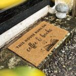 a doormat outside a door on gravel. doormat reads "this house runs on coffee and books"