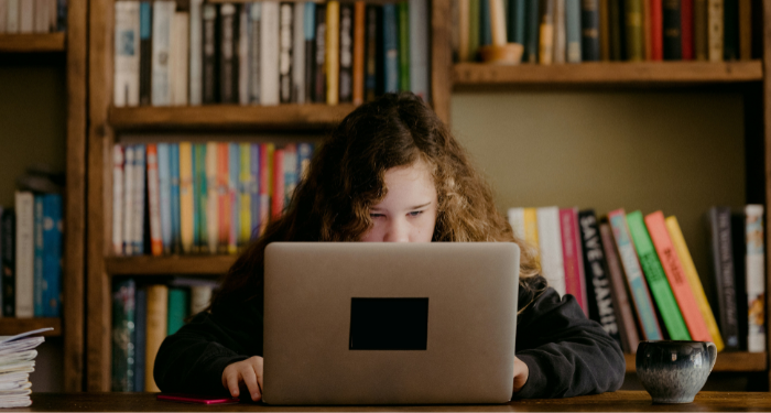 a young teen working on a laptop with bookshelves in the background