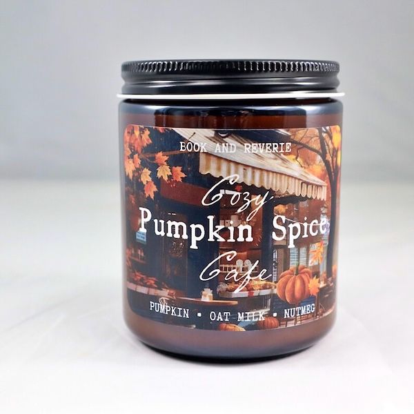 amber glass candle with a label containing a photographed image of a cafe storefront. Text on top of the image reads "Cozy Pumpkin Spice Cafe"