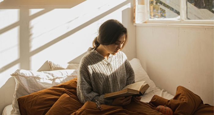 fair-skinned woman reading in bed with fall decorations around her