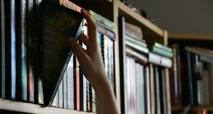 hand pulling book off library shelf.jpg.optimal