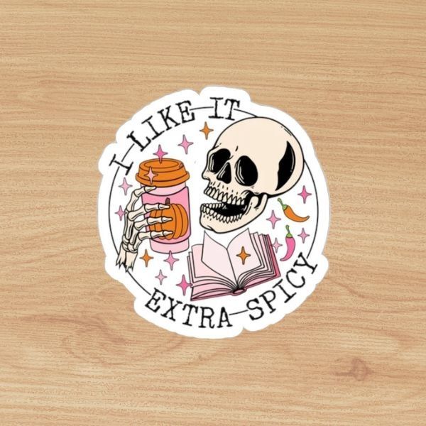 sticker of a skeleton holding a paper coffee cup with a pumpkin on the paper sleeve. Text bordering the design reads "I like it extra spicy"