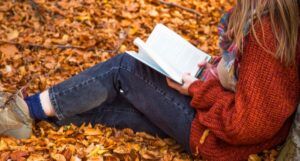 a child reading a book in a pile of leaves while leaning against a tree