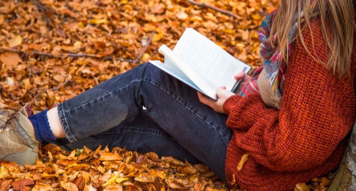 a child reading a book in a pile of leaves while leaning against a tree