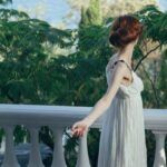 a white woman in a white empire waist dress gazing out at trees