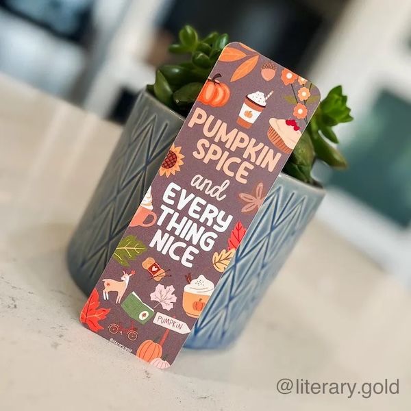 brown bookmark with several graphics of fall-themed items, like pumpkins, cups of coffee, books, and leaves. Text in the center reads Pumpkin Spice and Everything Nice