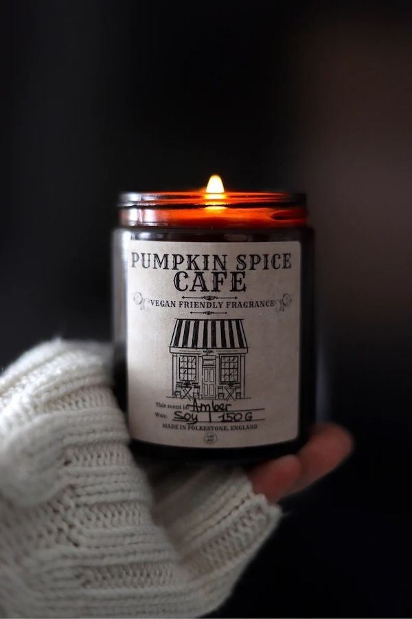 an amber glass candle with a black and white label containing an image of a cafe with text above it that reads "Pumpkin Spice Cafe"