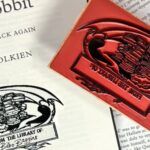 title page of The Hobbit stamped with a stamp of a dragon curled around a stack of books and the text "From the Library of: Bilbo Baggins"