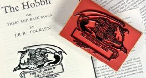 title page of The Hobbit stamped with a stamp of a dragon curled around a stack of books and the text "From the Library of: Bilbo Baggins"