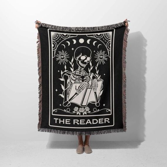 image of a person holding up a fringed throw blanket with a tarot card of a skeleton reading titled The Reader