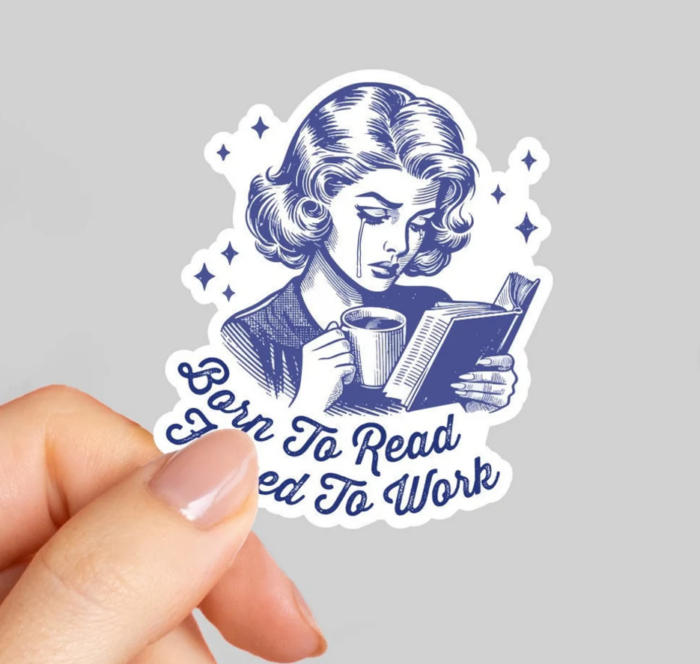 a hand holding a sticker that says "born to read, forced to work"