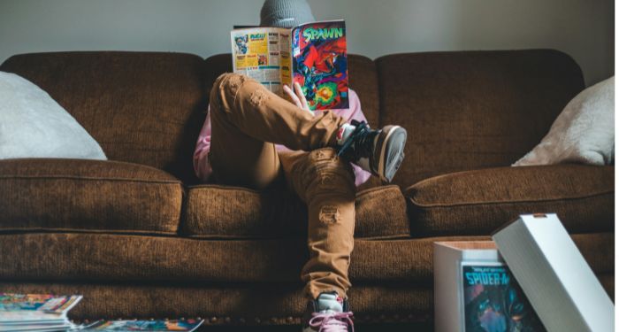 Young man sitting on sofa and reading comics magazine.jpg.optimal