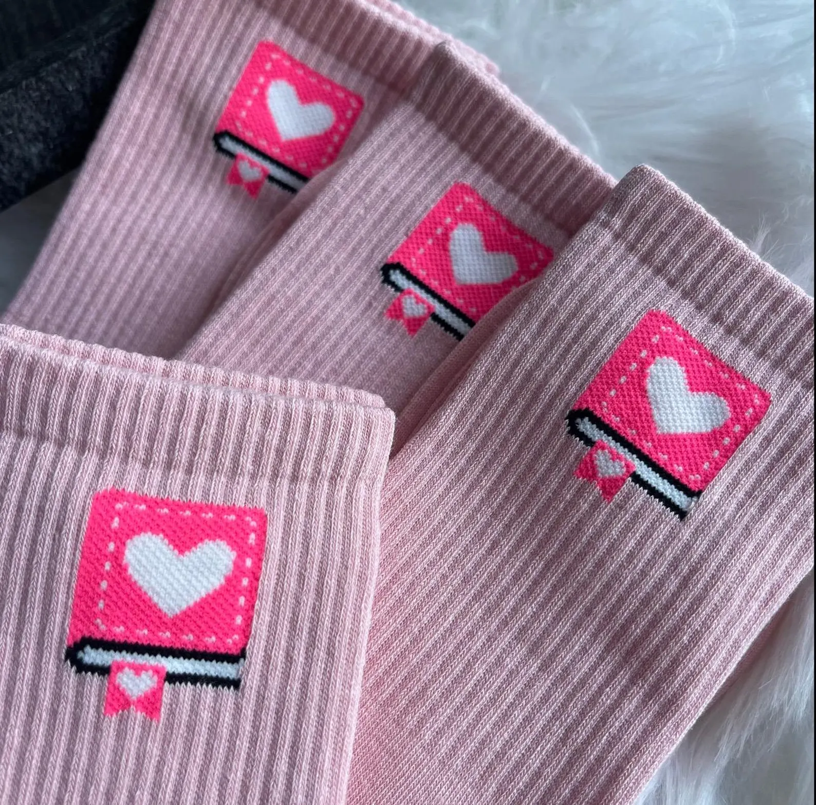 Image of the tops of four pairs of pink socks. All of them have a small book on them. 