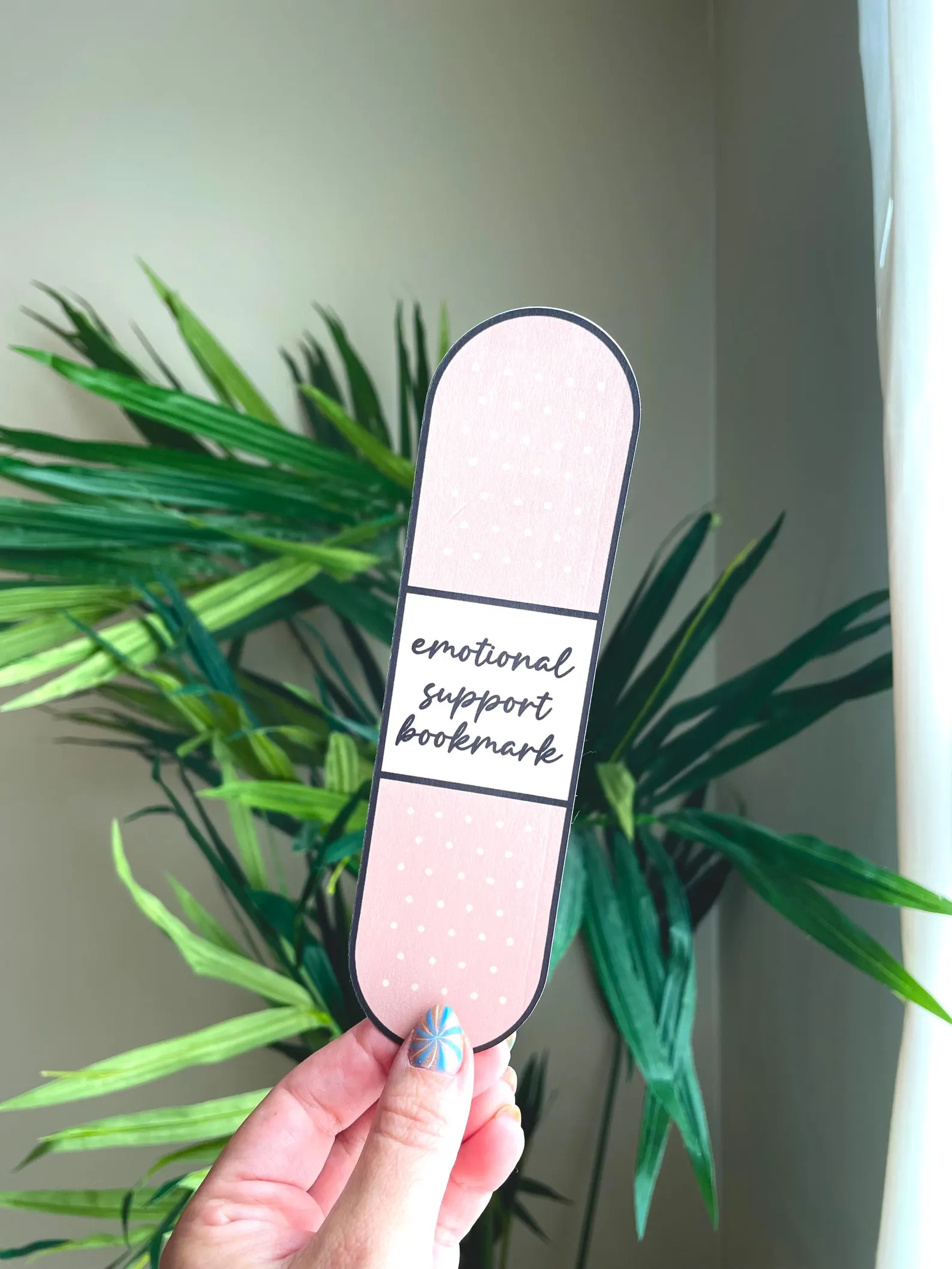 Image of a bookmark in the shape of a bandaid. It reads "emotional support bookmark" in the middle.