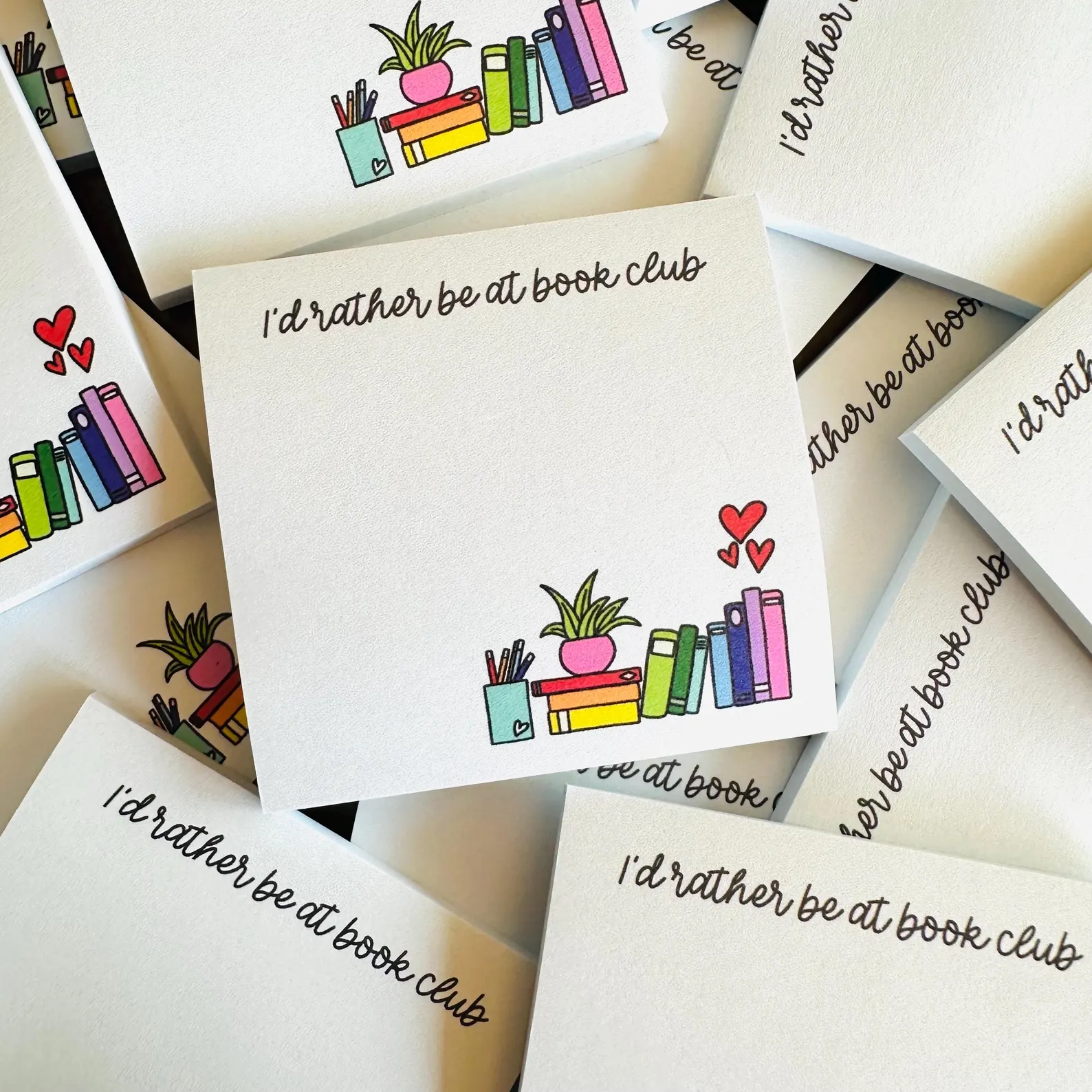 Image of a sticky note pad that says I'd rather be at book club" in cursive font. There are colorful books at the bottom. 