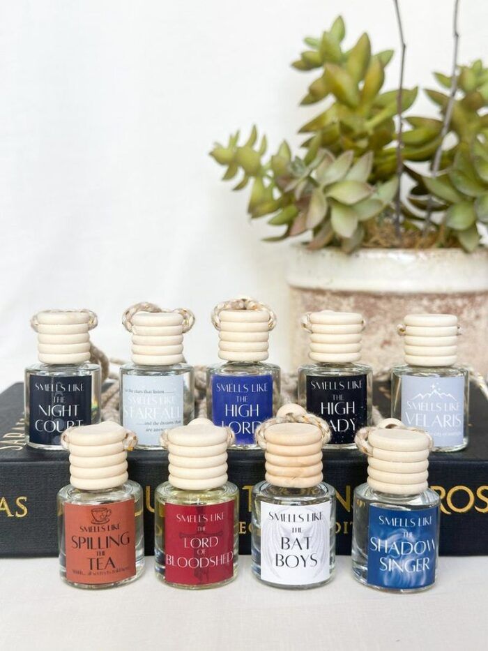 image of a plant behind several small bottles with canvas-rope  type toppers. The labels read things like "smells like the night court," and "smells like the high lady."