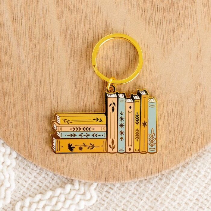 gold key ring with a charm depicting stacks of books- some horizontal, some verticle, in pastel colors with gold leaf designs on the spine 