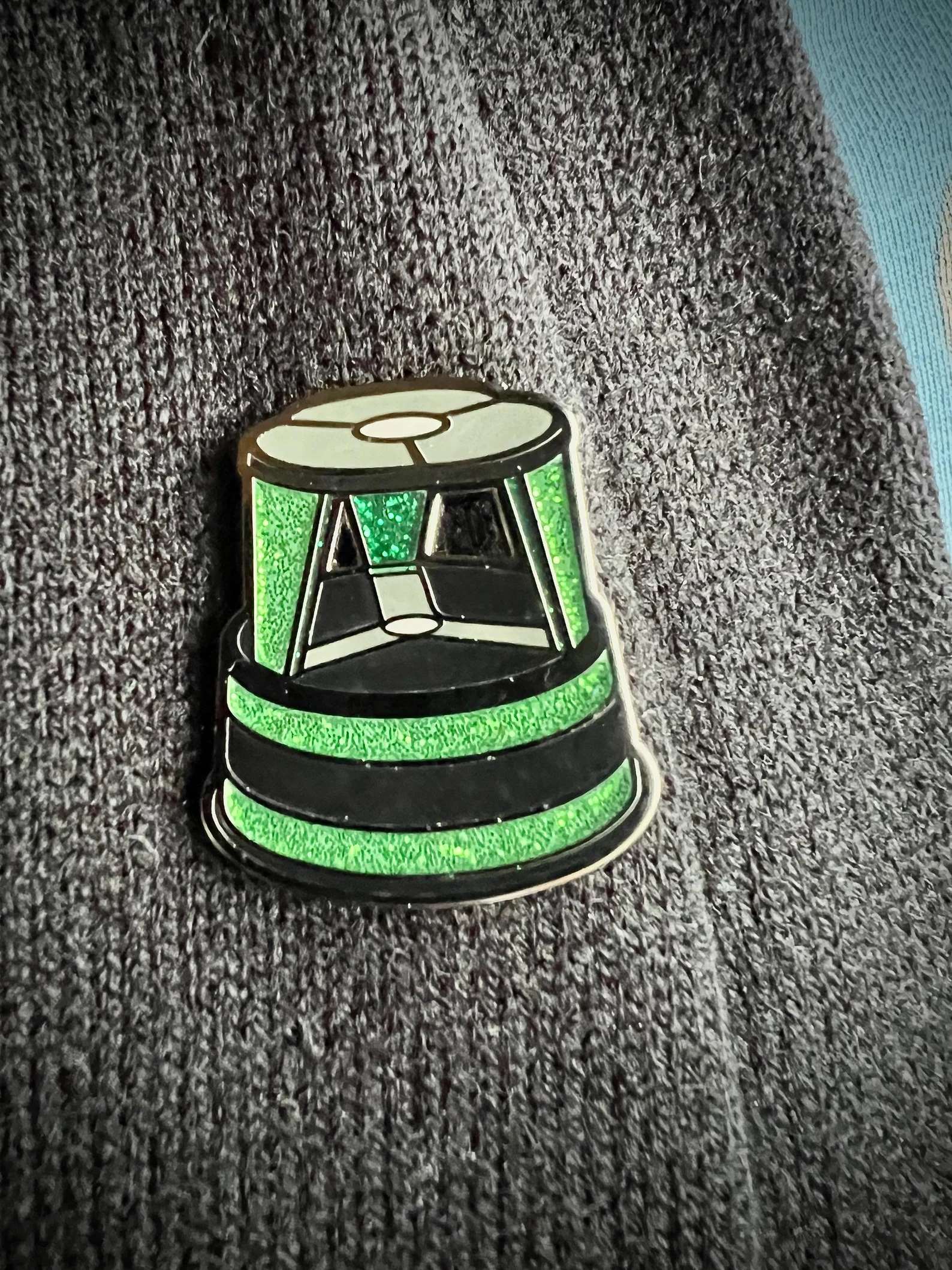 Image of an enamel pin that is in the design of a green library stool. 