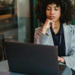 light-skinned Black woman with big, curly hair on a laptop at a coffee shop