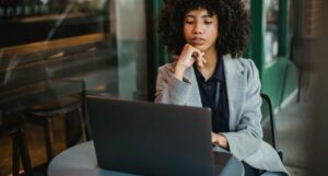 light-skinned Black woman with big, curly hair on a laptop at a coffee shop