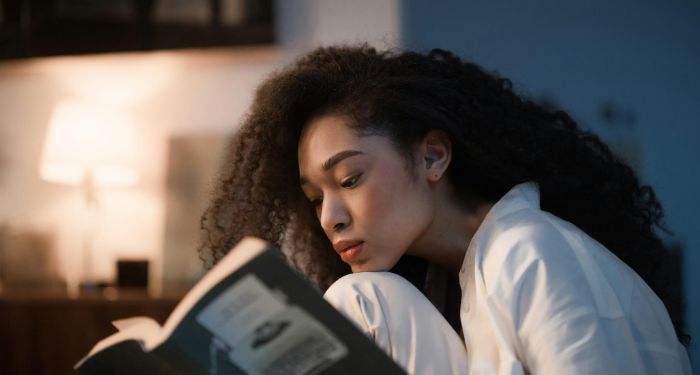 light-skinned Black woman with big, kinky hair reading with her chin resting on her knee