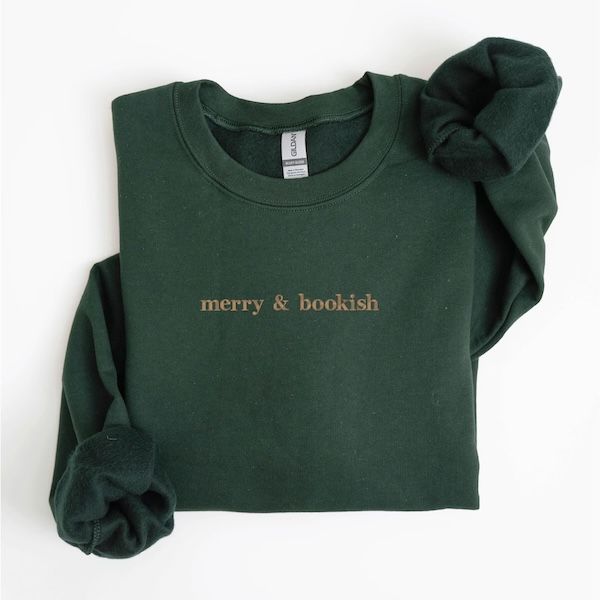 a forest green crewneck sweater with text on the front that reads "merry & bookish"