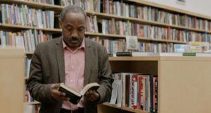 older, brown-skinned Black man reading in a library