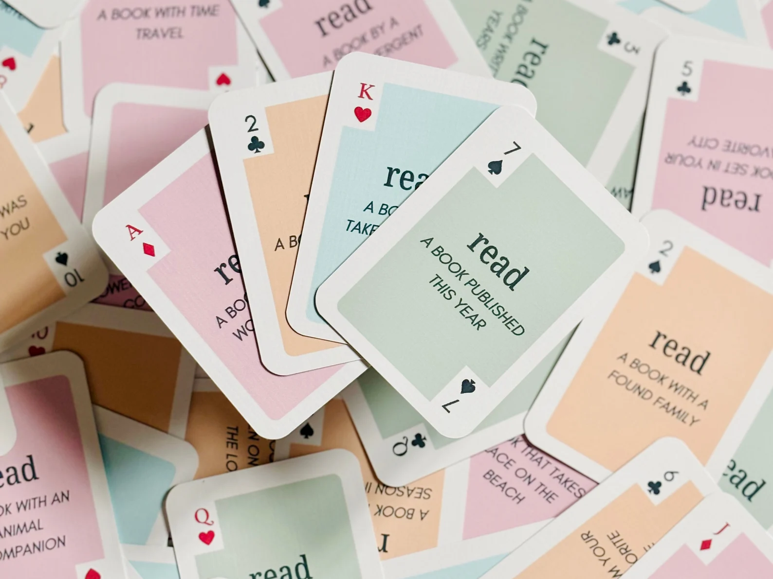 Image of a deck of colorful playing cards spread out. Each card has a theme for the kind of book someone should read, such as "read a book published this year."